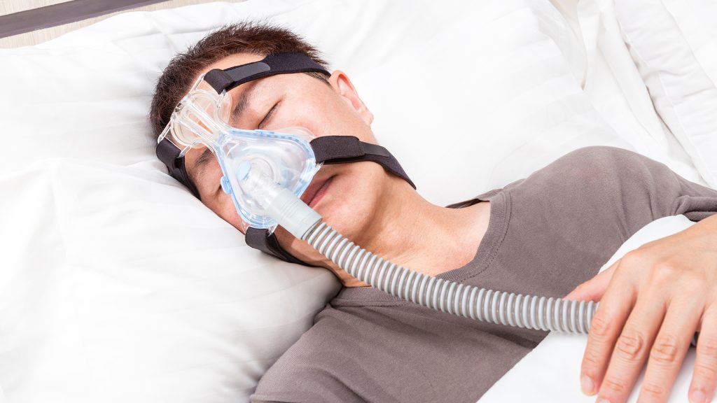 A person using a CPAP machine while comfortably positioned on an adjustable bed